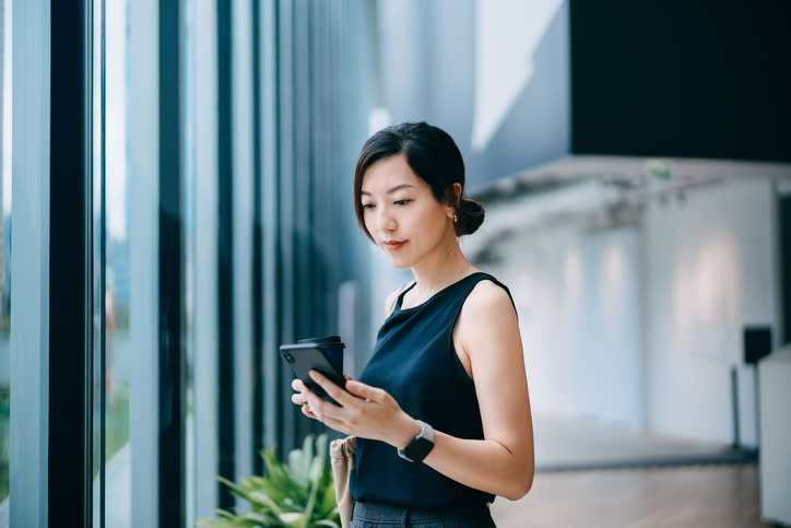 Woman in a sleeveless top using a smartphone by a window-lined corridor