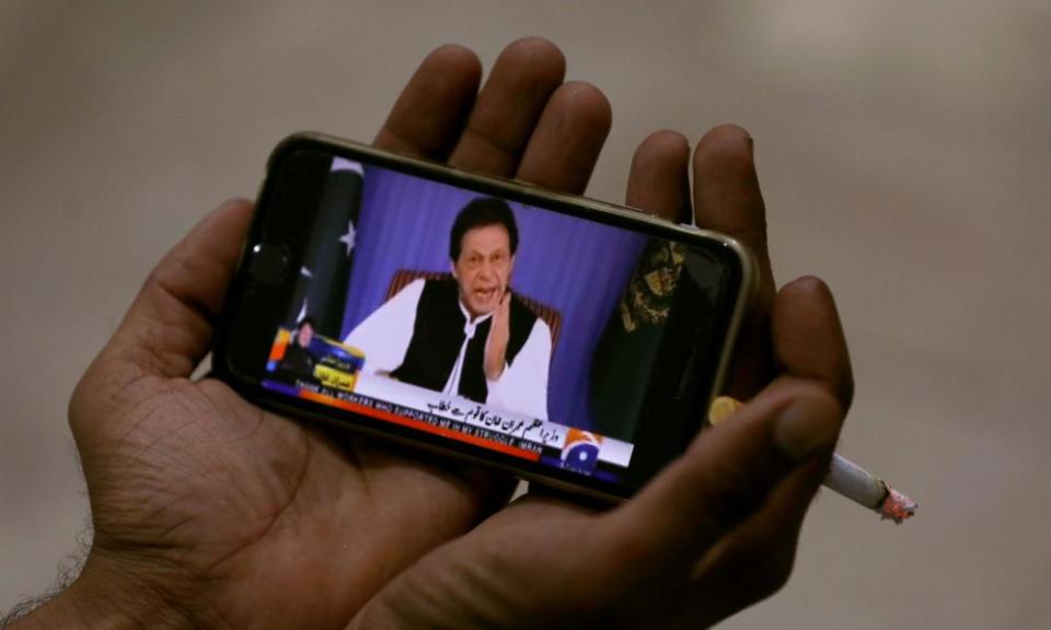 A man holds a phone showing Imran Khan speaking to the nation in his first televised address