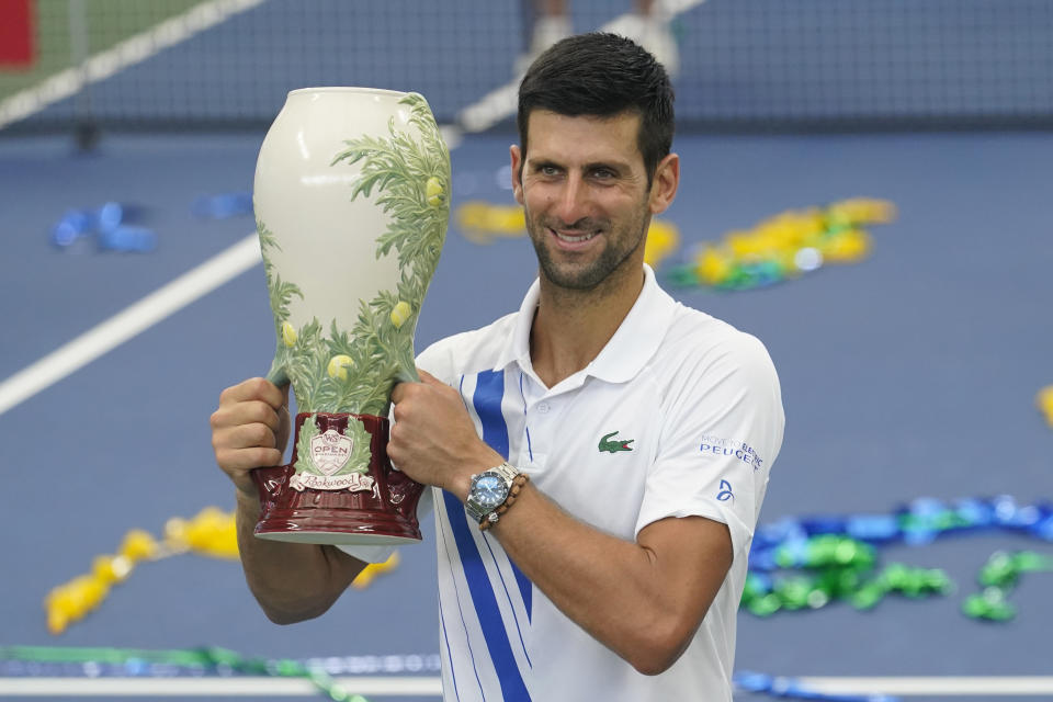 Novak Djokovic, of Serbia, front, holds his winning trophy after winning his match with Milos Raonic, of Canada, at the Western & Southern Open tennis tournament Saturday, Aug. 29, 2020, in New York. (AP Photo/Frank Franklin II)