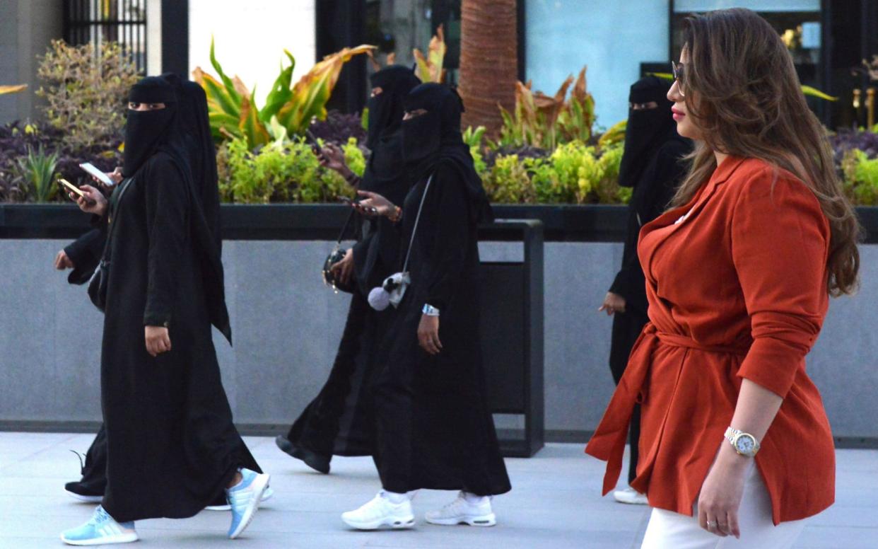 Saudi human resources professional Mashael al-Jaloud, 33, walks in western clothes past women wearing niqab, an Islamic dress-code for women, at a commercial area in the Saudi capital Riyadh - AFP