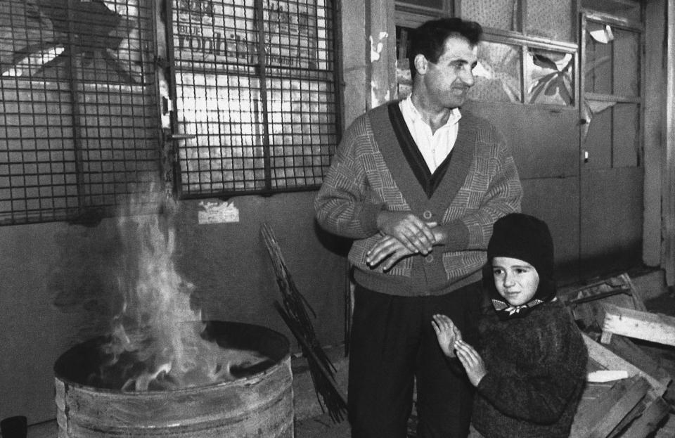 FILE - A father and his son stand in front of a destroyed store warming themselves up on an open fire in downtown Sarajevo, Wednesday, Oct. 14, 1992. For nearly four years, Sarajevo’s roughly 350,000 residents were trapped and faced daily shelling and sniper attacks. Cut off from regular access to electricity, heat and water, they survived on limited humanitarian aid from the United Nations while drinking from wells and foraging for food. (AP Photo/Hansi Krauss, File)