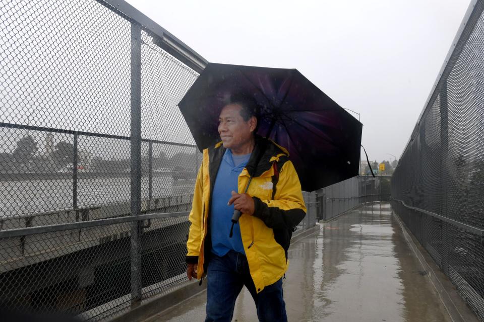 Raul Garcia Lopez of Oxnard walks on the Lewis Road bridge near the Camarillo Metrolink station to get to work as rain falls on Wednesday, Jan. 4, 2023.