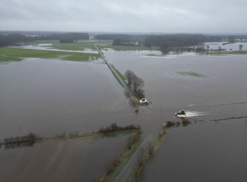 A tractor drives over a flooded road in the flood zone. After the River Ems burst its banks, many areas are under water. Lars Penning/dpa