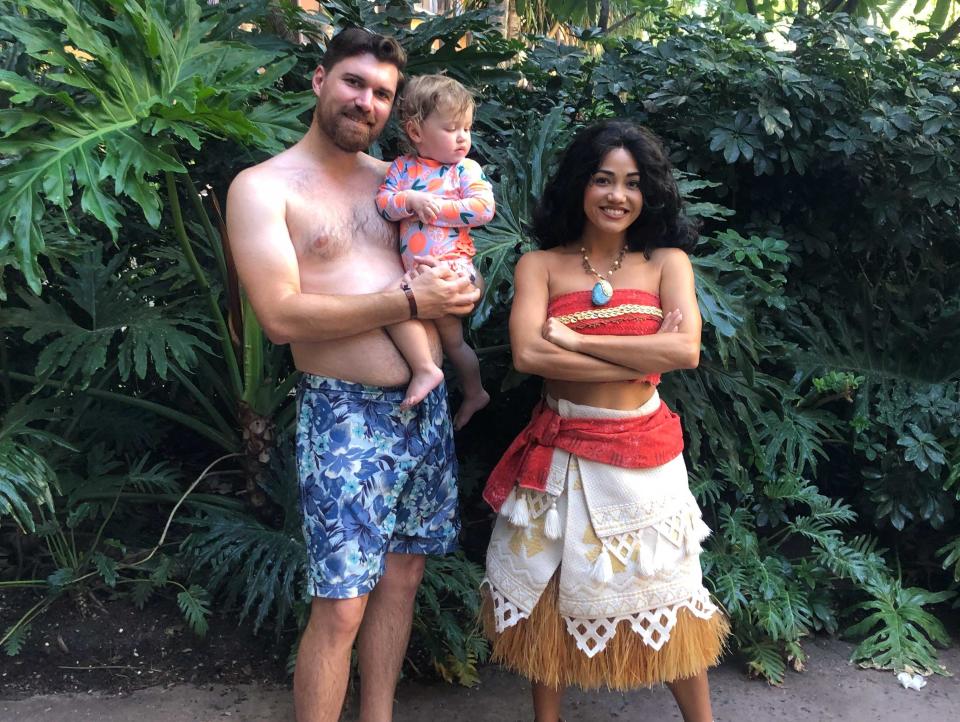 A man holding his baby posing with the Disney character, Moana.