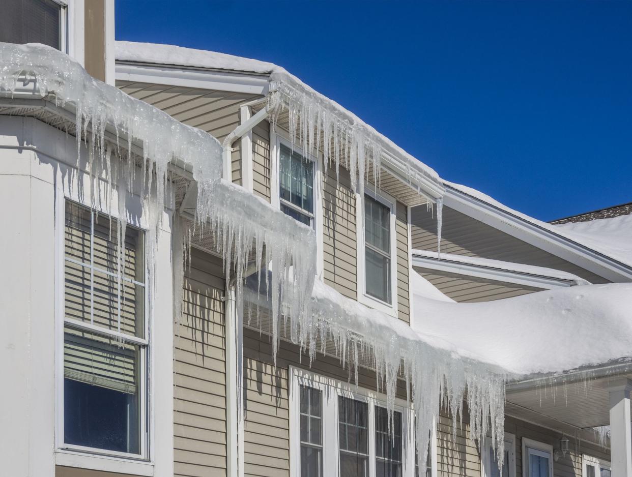Ice frozen in the gutters on the roof of a house with long icicles.