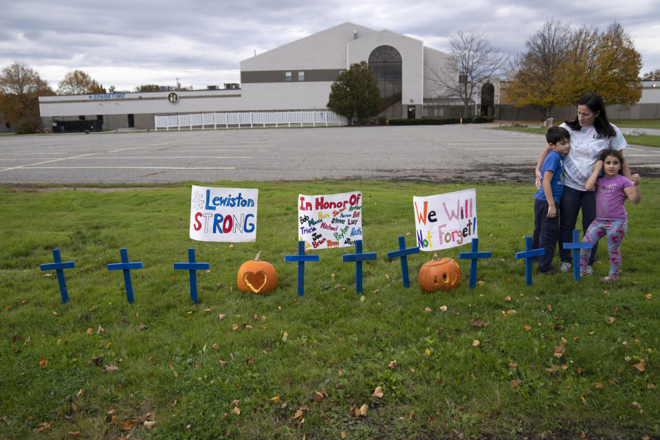 Bre Allard holds her children, Zeke and Lucy, after they set signs and crosses outside Sparetime Bowling Alley to show support for the community in the wake of this week's mass shootings, Saturday, Oct. 28, 2023, in Lewiston, Maine. The residents of Lewiston are embarking on a path to healing after a man suspected of killing several people earlier this week was found dead. The bowling alley was renamed in 2021 to Just-In-Time Recreation. (AP Photo/Robert F. Bukaty)