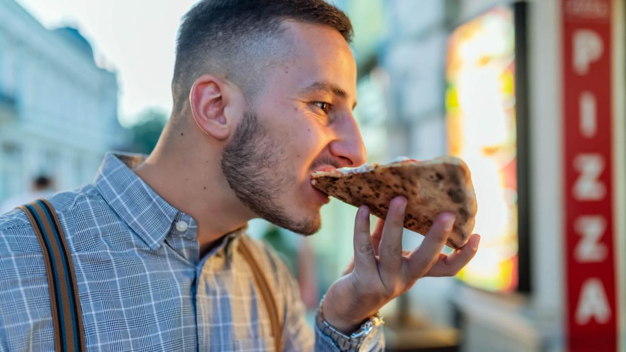 Handsome Teenager Enjoying a Big Slice of Pizza in the City Street During a Night.