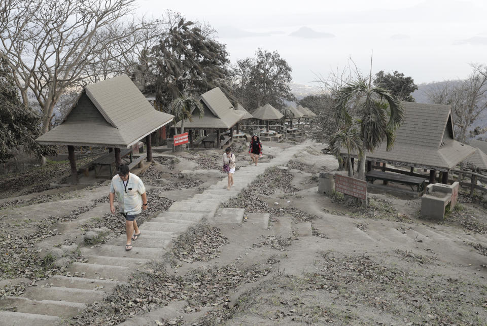 People walk along a park covered in volcanic-ash at a town near Taal volcano in Tagaytay, Cavite province, southern Philippines on Sunday Jan. 19, 2020. Philippine officials said Sunday the government will no longer allow villagers to return to a crater-studded island where an erupting Taal volcano lies, warning that living there would be "like having a gun pointed at you." (AP Photo/Aaron Favila)