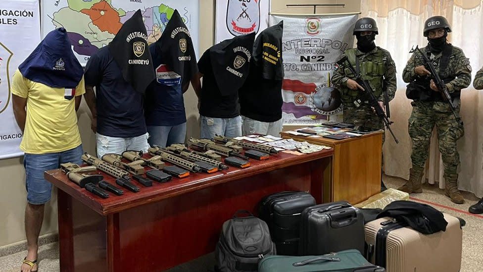 La policía de Paraguay muestra a varios detenidos encapuchados frente a una mesa con armas y material ilícito incautado.