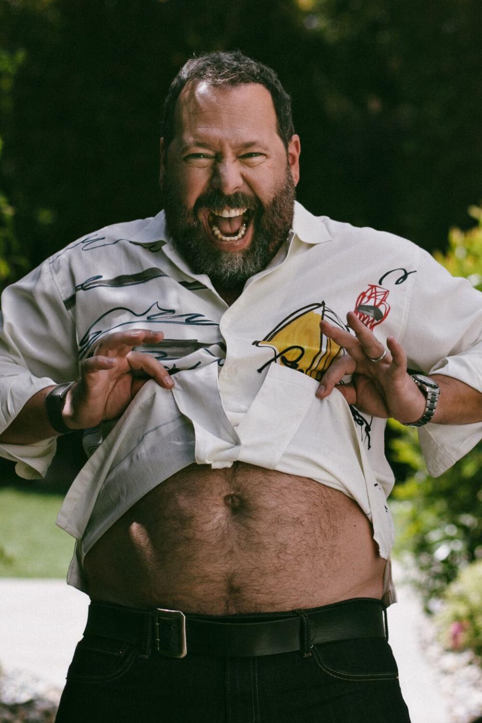 Bert Kreischer lifts his shirt, revealing his belly, and grins.