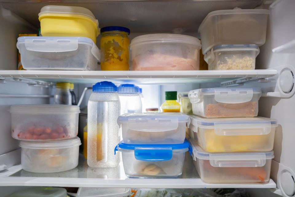 A refrigerator filled with assorted plastic containers holding various food items, including leftovers, fruits, and liquids