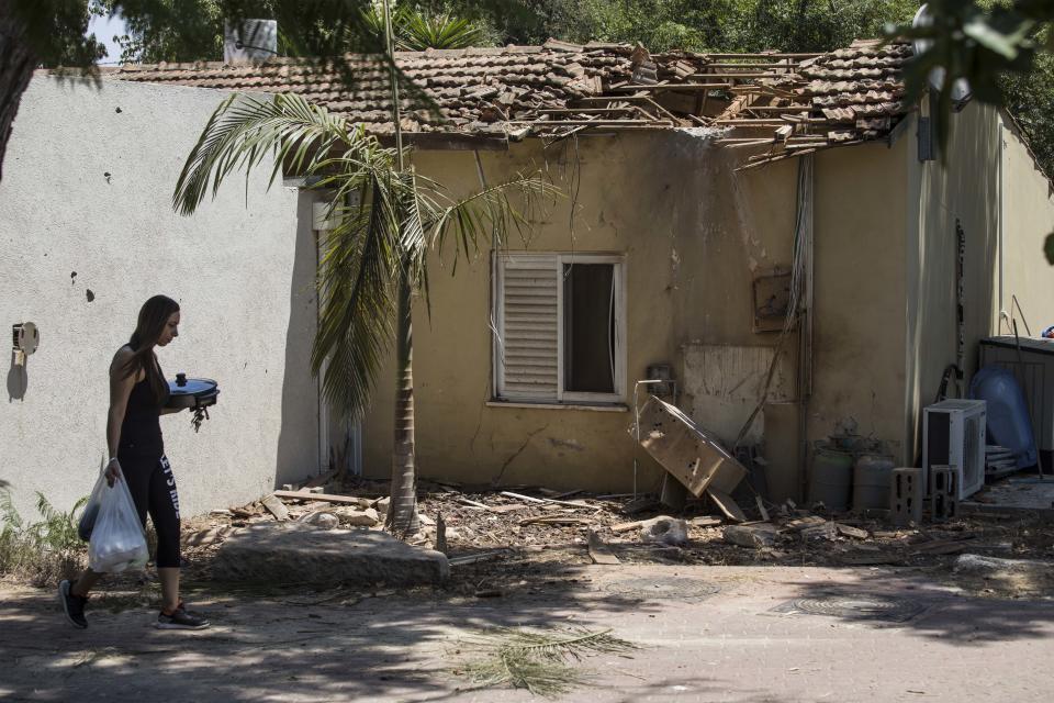 A woman walks by a house damaged by a missile fired from Gaza Strip, in a kibbutz near the Israel and Gaza border, Thursday, Aug. 9, 2018. Israeli warplanes struck dozens of targets in the Gaza Strip and three people were reported killed there, while Palestinian militants from the territory fired scores of rockets into Israel in a fierce burst of violence overnight and into Thursday morning. (AP Photo/Tsafrir Abayov)