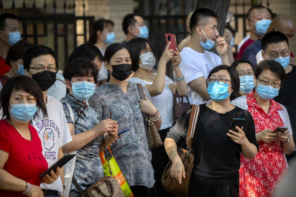 Relatives wearing face masks to protect against the new coronavirus watch as students line up for the first day of China's national college entrance examinations, known as the gaokao, in Beijing, Tuesday, July 7, 2020. China's college entrance exams began in Beijing on Tuesday after being delayed by a month due to the coronavirus outbreak. (AP Photo/Mark Schiefelbein)