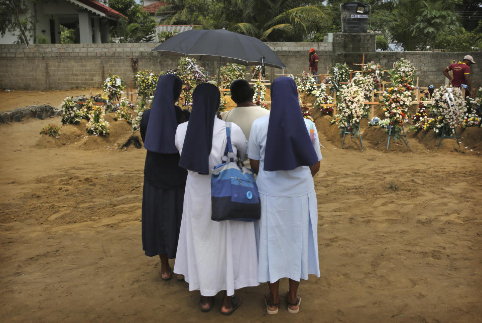 FILE - In this Thursday, April 25, 2019 file photo, Catholic nuns stand with a relative of a victim of Easter Sunday's bomb blast at St. Sebastian Church, at a mass burial site in Negombo, Sri Lanka. Roughly 250 people died in six coordinated suicide bombings that ripped through Sri Lanka on Easter Sunday. (AP Photo/Manish Swarup, File)