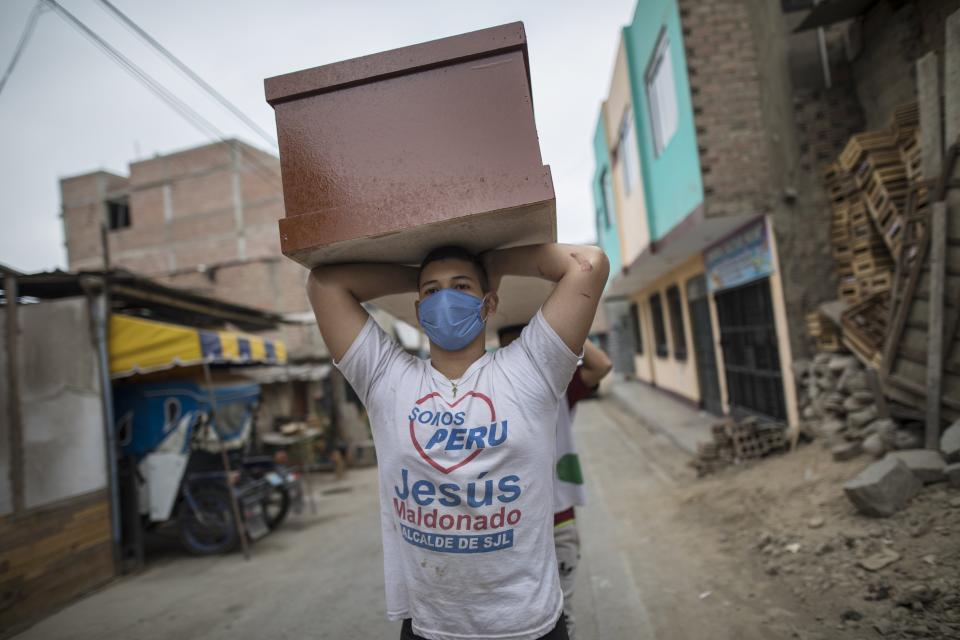 Un trabajador, un migrante de Venezuela, lleva un ataúd recién hecho para víctimas de COVID-19 a un almacén en una fábrica de ataúdes en el barrio Juan de Lurigancho de Lima, Perú, el jueves 4 de junio de 2020. Como el número de COVID -19 muertes en Perú aumenta rápidamente, el país sudamericano se está convirtiendo en uno de los epicentros del brote del virus en América Latina. (AP Foto/Rodrigo Abd)