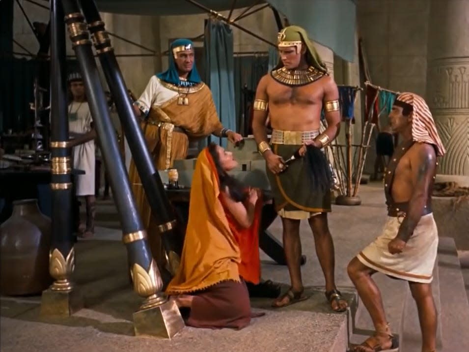 A woman is on her knees begging a man dressed as an Egyptian holding a whip.