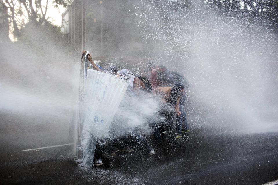 Manifestantes antigubernamentales se cubren de un chorro de agua disparado por la policía antidisturbios en Caracas, Venezuela, el viernes 28 de febrero de 2014. (Foto AP/Rodrigo Abd)