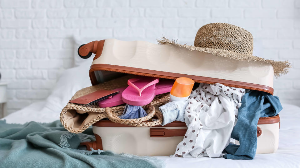 Open suitcase on a bed filled with holiday clothes