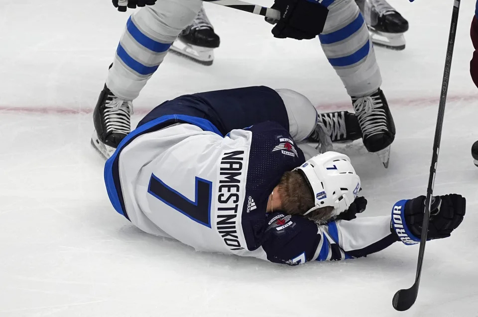 Winnipeg Jets center Vladislav Namestnikov (7) falls to the ice after taking a slap shot to the face in the third period of Game 4 of an NHL Stanley Cup first-round playoff series against the Colorado Avalanche, Sunday, April 28, 2024, in Denver. (AP Photo/David Zalubowski)