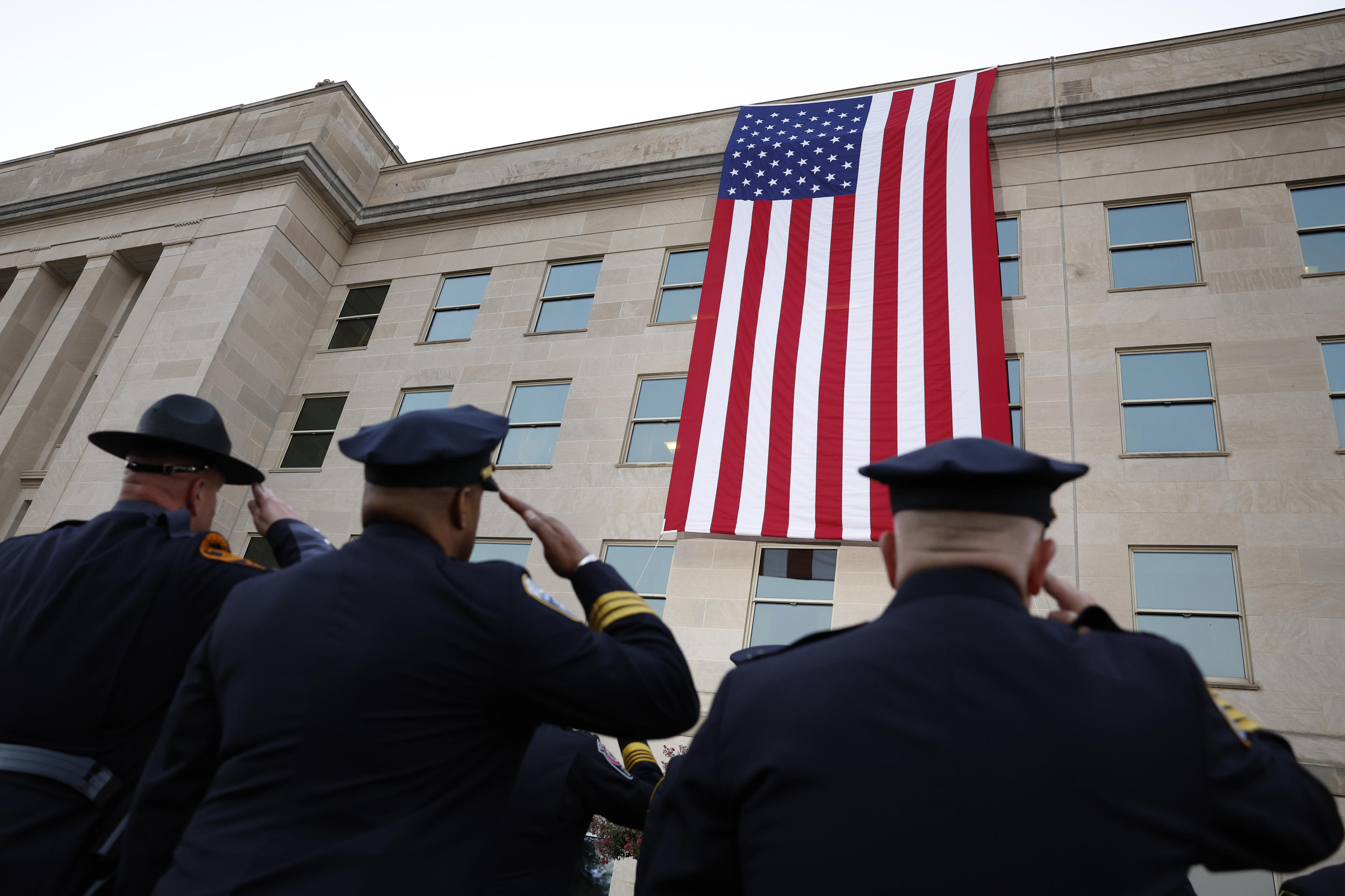 Military members and first responders watch as an American flag is unfurled at the Pentagon in Arlington, Virginia, on Wednesday to commemorate the 23rd anniversary of the Sept. 11 terrorist attacks.