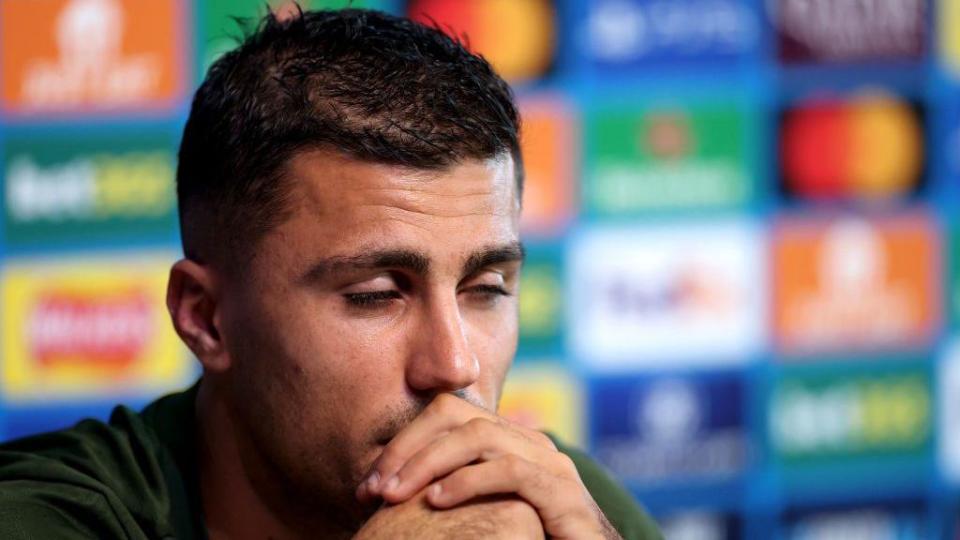 Rodri holds his hands to his face during a press conference