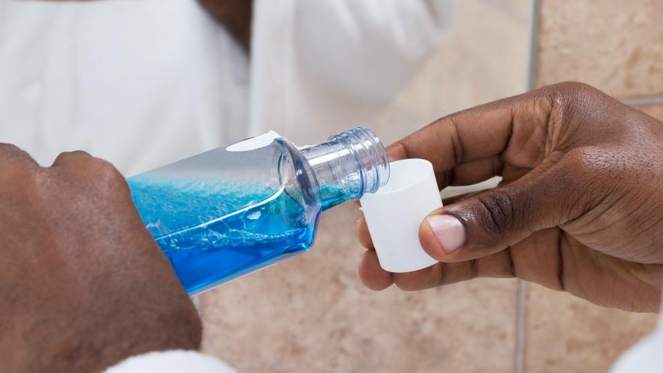 Close-up Of Person Hands Pouring Blue Mouthwash Into Bottle Cap.