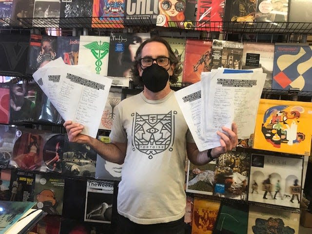 Andrew Schaer, owner of Hear Again Records in downtown Gainesville, shows a few handfuls of pages of customers and business owners opposed to the city imposing paid downtown parking.