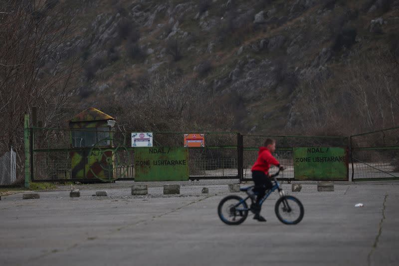 A child rides a bicycle next to a checkpoint at a military base, in Gjader