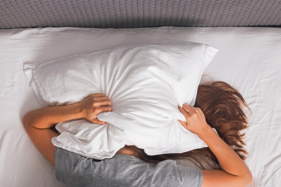 Woman lying in bed and covering her head with pillow. Struggling from insomnia, noise or early morning get up.