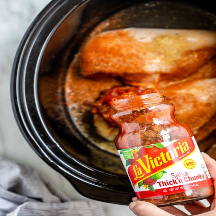 Someone pouring salsa onto chicken breasts in a slow cooker.