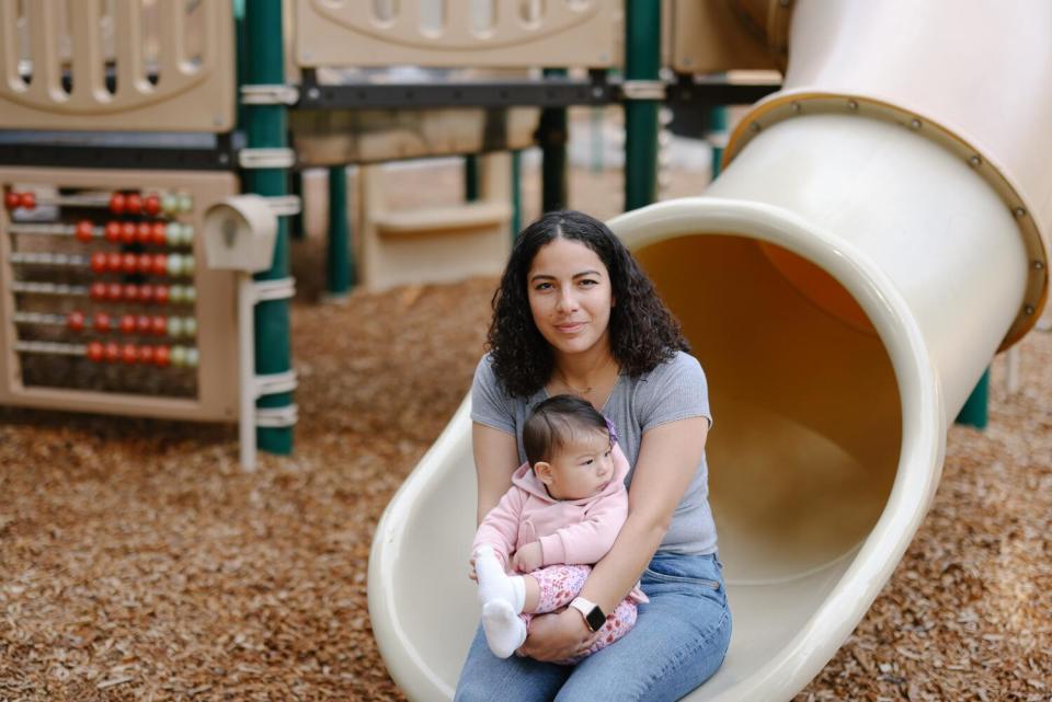 A woman sits with a baby on the edge of a slide.