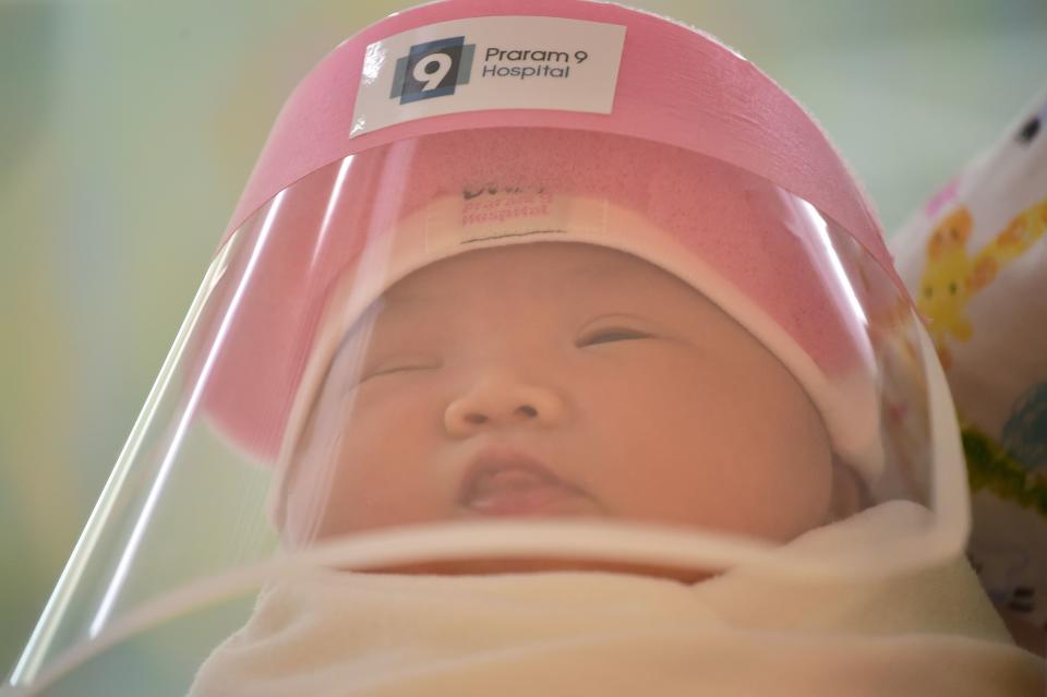 This photo taken through a glass window at a maternity ward shows a newborn baby wearing a face shield, in an effort to halt the spread of the COVID-19 coronavirus, at Praram 9 Hospital in Bangkok on April 9, 2020. (Photo by Lillian SUWANRUMPHA / AFP) (Photo by LILLIAN SUWANRUMPHA/AFP via Getty Images)