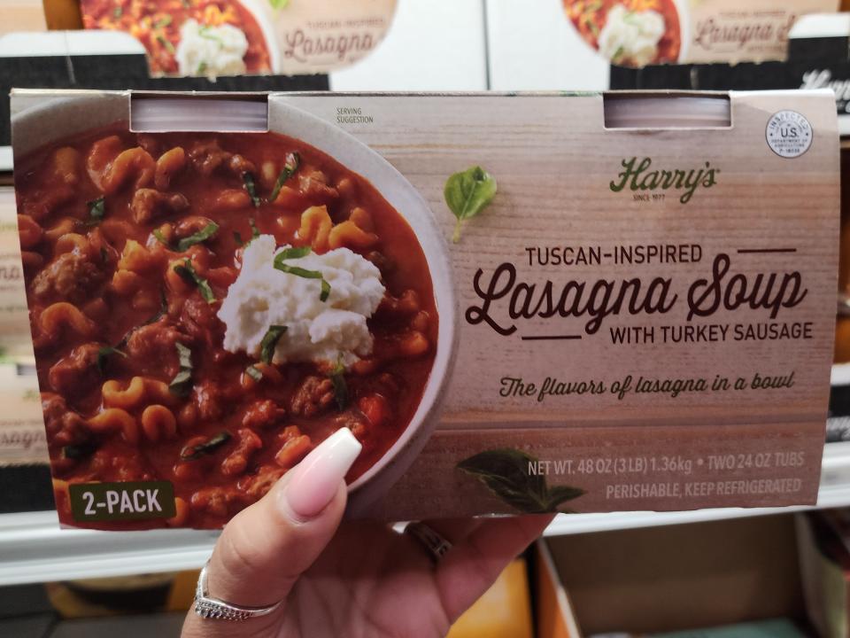 A hand holding up a container of Harry's lasagna soup