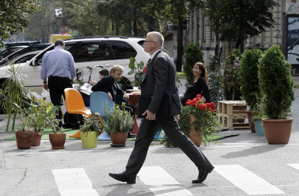 A man crosses a street past people participating in a PARK(ing) Day event in Riga