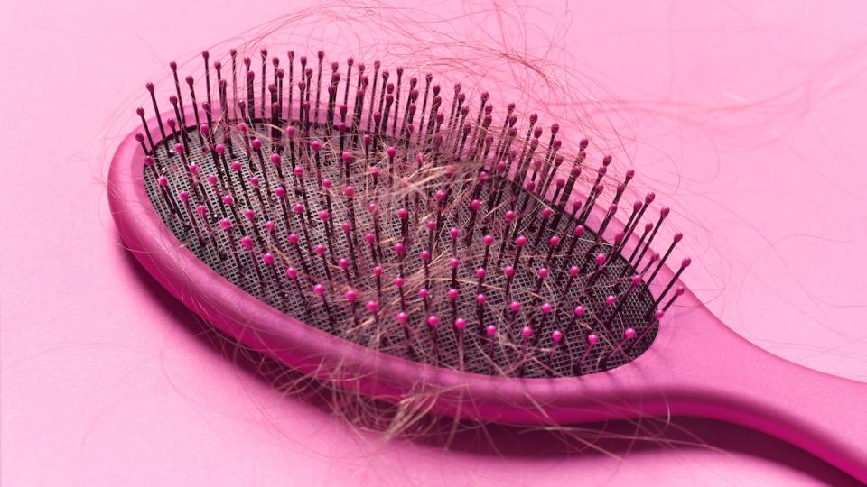 Close up of a brush with loose hair in it on a pink background