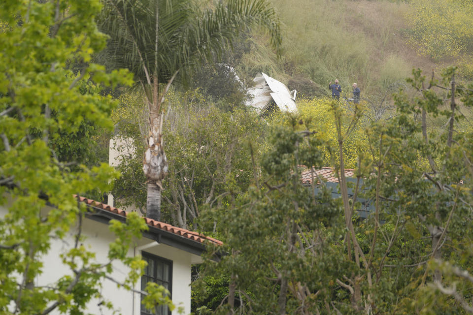 National Transportation Safety Board investigators inspect a downed plane on a steep hill above a home on Beverly Glen Circle in Los Angeles, Sunday, April 30, 2023. Fire department officials said a person was found dead following an intensive search for the single-engine airplane that crashed in a foggy area Saturday night. (AP Photo/Damian Dovarganes)