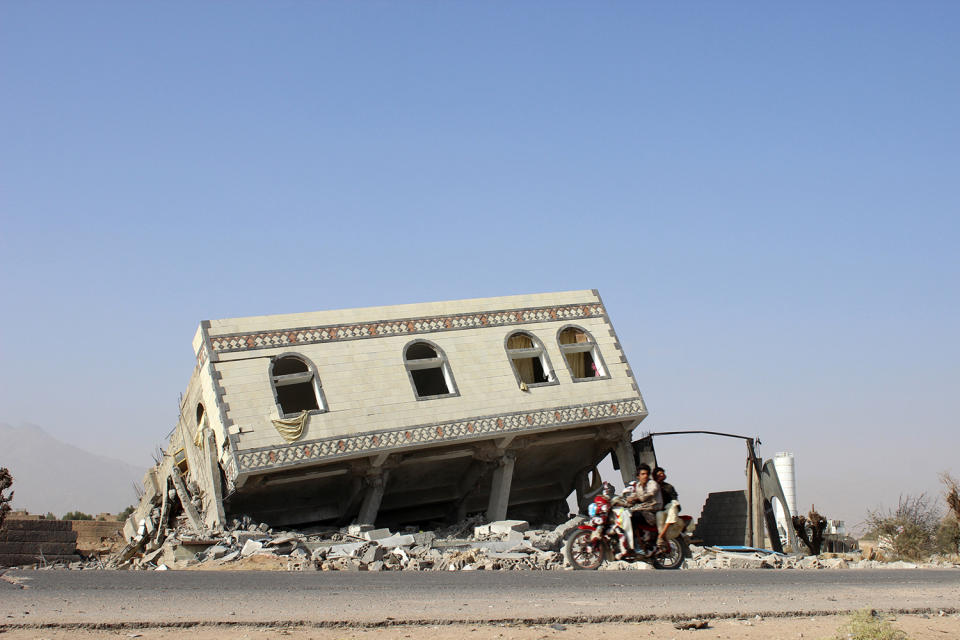 People ride a motorbike past a collapsed building