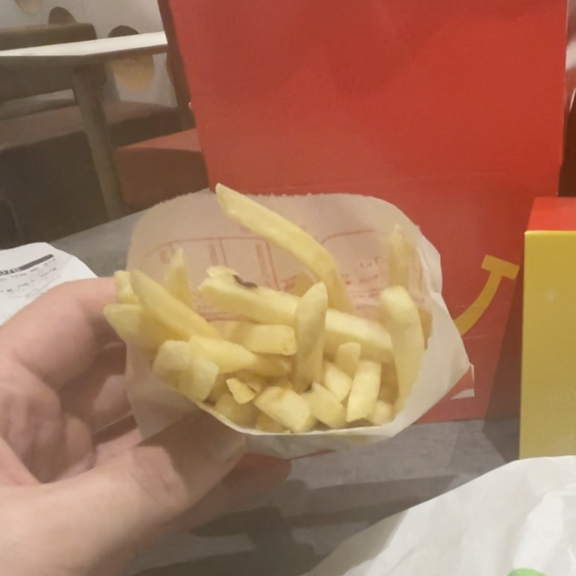 Person holding a carton of fries with fast-food packaging in the background