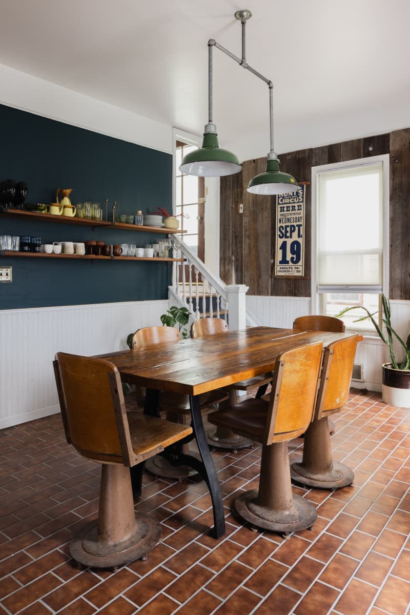 Wood and metal table and chairs in center of dining area with brick-like subway floor and wood paneled wall.