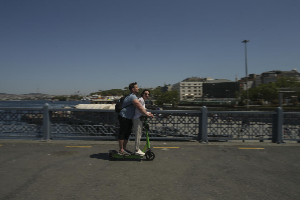 People ride a scooter on the Galata Bridge over the Golden Horn in Istanbul, Friday, May 14, 2021.Turkey is in the final days of a full coronavirus lockdown and the government has ordered people to stay home and businesses to close amid a huge surge in new daily infections. But millions of workers are exempt and so are foreign tourists. Turkey is courting international tourists during an economic downturn and needs the foreign currencies that tourism brings to help the economy as the Turkish lira continues to sink. (AP Photo/Emrah Gurel)