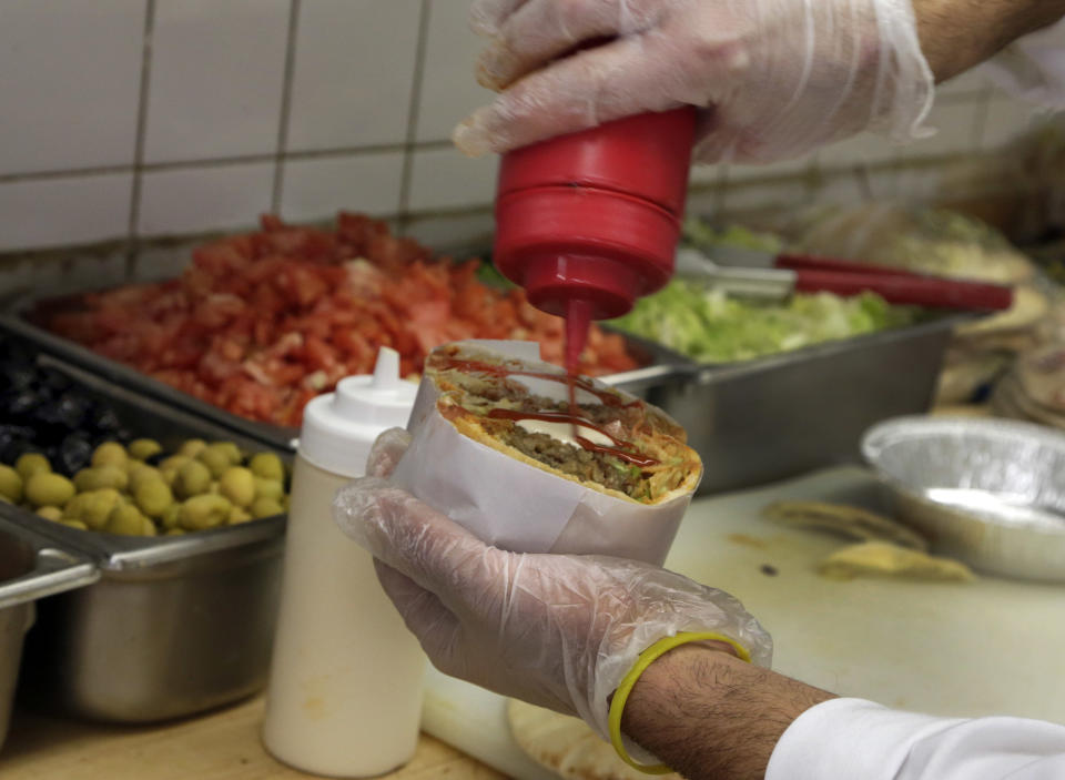 In this Nov. 21, 2013 photo, Amine Dekkar dresses a stuffed pita sandwich in the tiny upstairs deli at Kalustyan's Indian/Middle Eastern spice and specialty food shop in New York. They dole out hummus, falafel, moussaka, stuffed grape leaves, 16 types of olives, and more varieties of feta cheese than you’ll know what to do with. The not-so-little gem of a shop nestled into a row of like-minded stores on Lexington Avenue is known to New Yorker foodies, but off the map for most tourists. (AP Photo/Richard Drew)