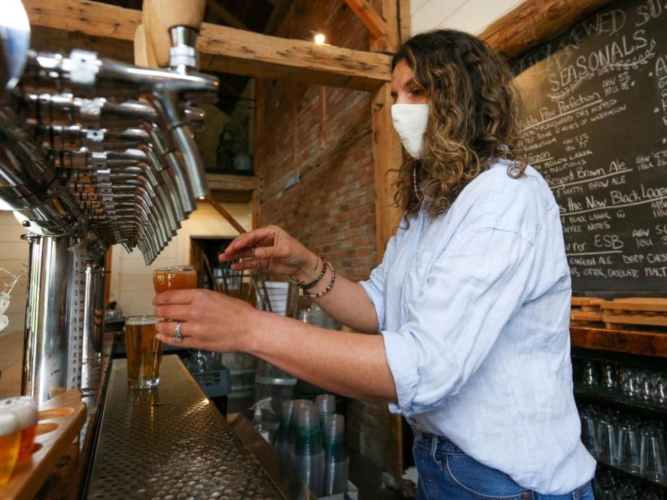 Parsons Brewing Company owner Samantha Parsons pours a beer at the brewery in Picton, Ont., earlier this year. The province is lifting capacity limits Monday at restaurants, gyms, casinos and some other locations where proof of vaccination is required.  (Lars Hagberg/Reuters - image credit)