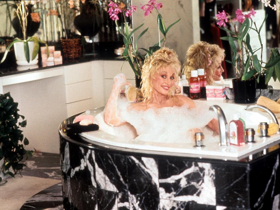 Dolly Parton in character as Shirlee Kenyon smiling in a marble bathtub.