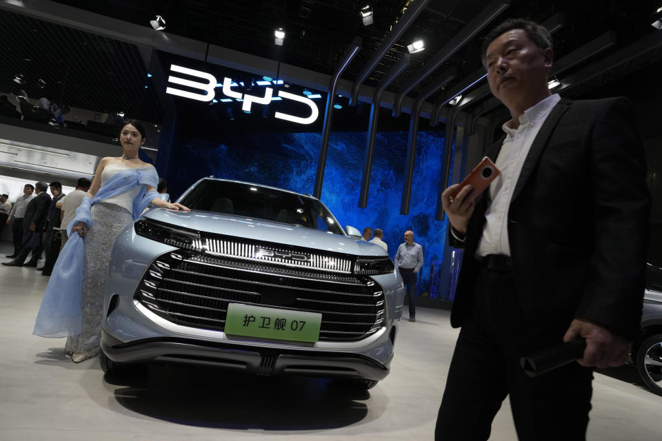 A model stands next to a car from BYD during the Shanghai auto show in Shanghai, on April 18, 2023. Threatened by possible shortages of lithium for electric car batteries, automakers are racing to lock in supplies of the once-obscure "white gold" in a politically and environmentally fraught competition from China to Nevada to Chile. General Motors Co. and the parent company of China's BYD Auto Ltd. went straight to the source and bought stakes in lithium miners, a rare step in an industry that relies on outside vendors for copper and other raw materials. (AP Photo/Ng Han Guan)