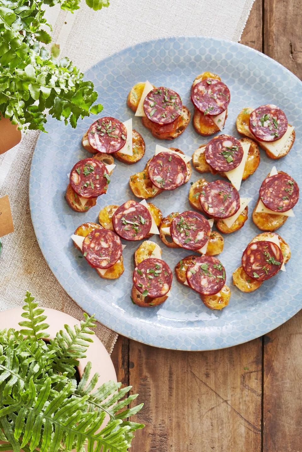 chorizo and manchego crostini arranged on a light blue plate and sprinkled with chopped herbs