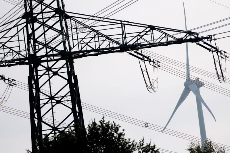 A wind turbine stands behind a high-voltage power line in a field. Energy-intensive companies need more support from the European Union, a group of large European industrial associations said in a statement released in Brussels on Tuesday. Hauke-Christian Dittrich/dpa