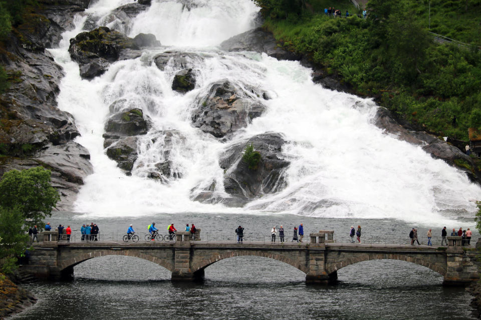 This June 5, 2019 photo shows people on a bridge at the foot of a waterfall in the town of Hellesylt, Norway. (AP Photo/Brian Witte)