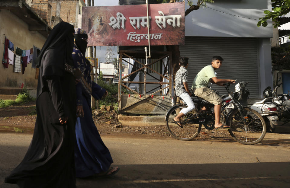 Muslim women walk past a board displaying the name of the Hindu nationalist group Sri Ram Sena Hindustan in a residential neighborhood in Belagavi, India, Oct. 7, 2021. Sri Ram Sena Hindustan denied that its members killed Arbaz Mullah and said the group was being targeted for "working for the benefit of Hindus." Its leader, Ramakant Konduskar, who calls himself a foot soldier in the battle to save Hinduism, said he is not against any religion but people should marry within their own. He considers "love jihad" a threat to society. (AP Photo/Aijaz Rahi)