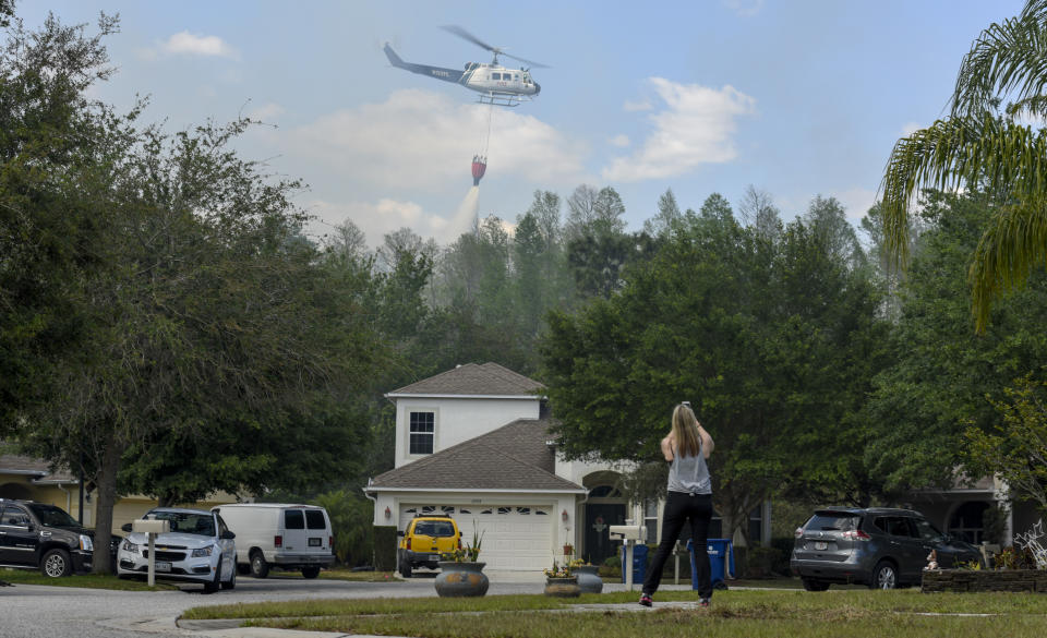 Suncoast Lakes resident Kristin Werner uses her cellphone to record a Florida Forest Service helicopter dropping water behind homes on the Silver Palm fire Tuesday, April 11, 2017, in Land O' Lakes. The Silver Palm Fire burned close to homes in the Suncoast Lakes subdivision Tuesday forcing residents to use garden hoses on vegetation and roofs around their property. (Chris Urso/The Tampa Bay Times via AP)