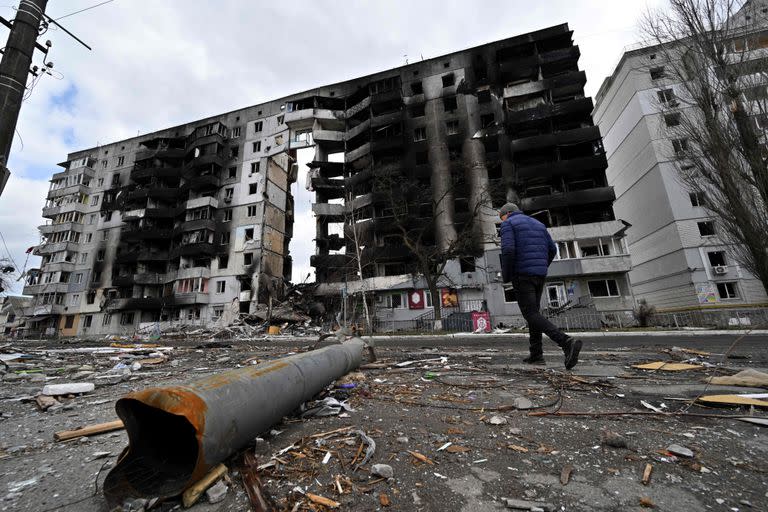 Un hombre pasa junto a un fragmento de artillería esparcido por una calle mientras camina junto a edificios destruidos en la ciudad de Borodyanka